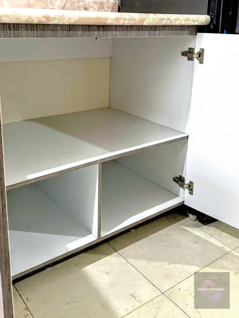 Módulo base de cocina con dos puertas abiertas, exhibiendo amplios entrepaños de melamina blanca diseñados para el soporte de baterías de cocina.